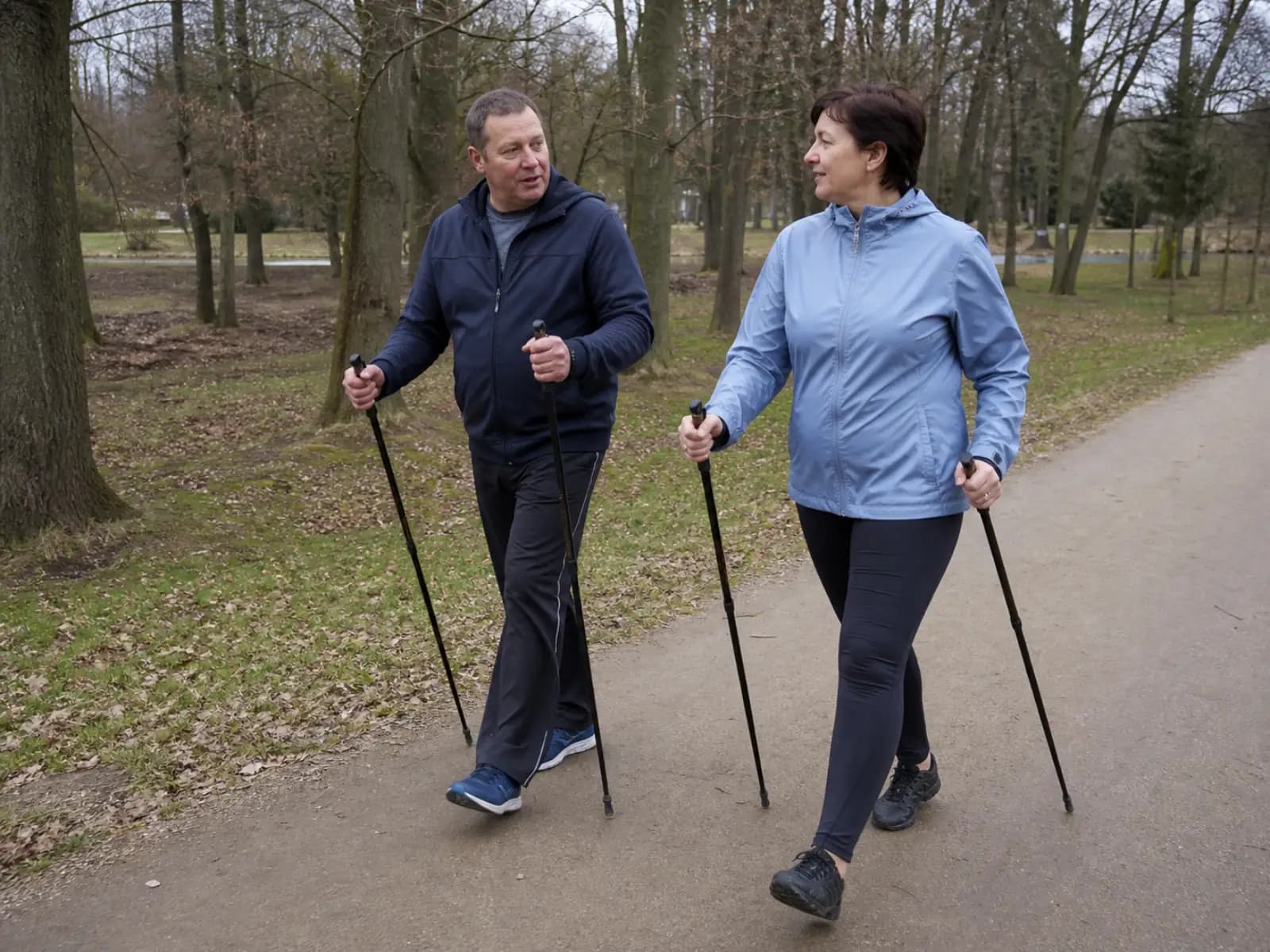 Para maszeruje z kijkami nordic walking po parkowej ścieżce